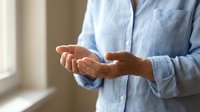 Senior man in light blue shirt holding cupped hands in protective gesture, symbolizing care, support and security in bright indoor setting.