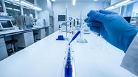 Scientist in blue gloves conducting chemical analysis with test tubes and laboratory equipment in modern research facility for pharmaceutical development.