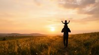 Father carrying young child on shoulders in golden wheat field at sunset, celebrating outdoor family bonding and parenting moments.