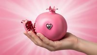 Hand holding pink pomegranate with heart symbol on radiant background for health and wellness concepts.