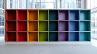 Colorful empty storage cubes in rainbow order against white wall with windows. Modern minimalist shelving unit featuring organized compartments for office or home organization.
