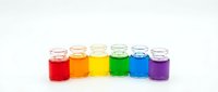 Six glass bottles filled with vibrant rainbow colored liquids arranged in row on white background for laboratory experiments and educational materials.