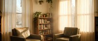Cozy reading corner with comfortable armchairs and bookshelf in warm sunlit living room with sheer curtains for home interior design and relaxation.