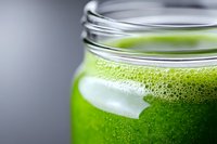 Fresh green smoothie or juice with foam in glass jar against dark background, close up view showing texture and bubbles. Healthy detox drink.