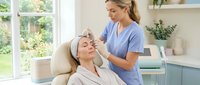 Professional beautician applying eyebrow treatment to relaxed female client in modern spa salon with natural lighting and clean aesthetic.