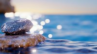 Zen stones balanced on water surface with golden sunlight reflections creating peaceful meditation and spa atmosphere for wellness relaxation concepts.