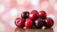 Fresh ripe cranberries scattered on reflective surface with soft pink bokeh background for holiday cooking and festive seasonal recipes.