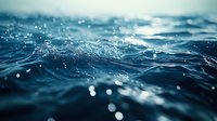 Macro shot of dark blue ocean waves with water drops and bokeh effect creating dreamy atmosphere. Dynamic seascape with splashing motion and soft focus background.