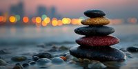 Balanced stack of zen stones on beach at sunset with blurred city lights creating peaceful meditation atmosphere.