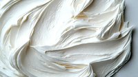Creamy white frosting swirls create soft textural waves and peaks, captured in macro detail against light background. Smooth buttercream texture for bakery and dessert designs.