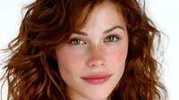 Young woman with natural makeup, freckles and wavy brown hair smiling warmly at camera against white background, expressing genuine happiness and confidence.
