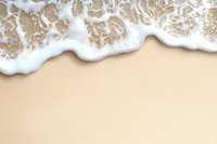 Gentle ocean wave with white foam washing up on smooth beige sand beach, creating natural border design at top of frame. For summer and beach themes.
