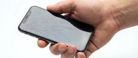 Caucasian male hand holding smartphone with cracked screen display against white background, showing device damage and repair needs for technology and insurance concepts.