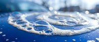 Close-up of water droplets forming heart shape on blue surface with bokeh lights background for romantic and love concepts in advertising materials.