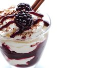 Layered dessert with fresh blackberries and chocolate sauce in glass cup, creamy parfait with berry compote and cinnamon stick garnish for cafe menu.