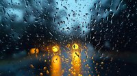 Rainy evening view through car windshield with water droplets, blurred traffic lights creating atmospheric golden bokeh effect against dark blue background.