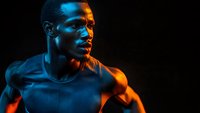 Athletic African American male in dark tank top illuminated by dramatic blue and orange lighting, creating strong contrast and mood for sports and fitness marketing.