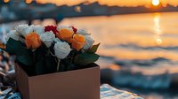 Fresh roses in wooden box against sunset ocean backdrop, orange and white blooms creating romantic coastal atmosphere with golden hour lighting and bokeh water reflections.