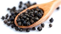 Black peppercorns in wooden spoon on white background, aromatic spice for cooking and seasoning, culinary ingredient for kitchen and restaurant use.