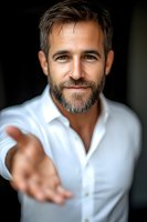Confident mature Caucasian businessman with gray hair and beard wearing white shirt extends hand for handshake against dark background, welcoming professional portrait.