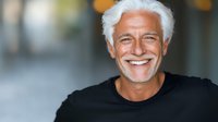 Mature Caucasian man with white hair and beard wearing black t-shirt showing genuine smile against blurred background. Positive aging and wellness concept.