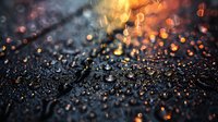 Glowing orange and yellow bokeh lights reflect on wet dark surface with water drops creating magical atmospheric mood. Blurred background with sparkles.