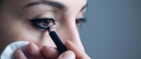 Young woman applying black eyeliner pencil to lower eyelid in close-up beauty makeup routine for cosmetics and personal care tutorials.