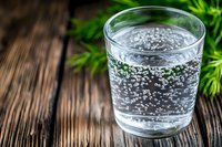 Glass of sparkling mineral water with bubbles on rustic wooden table with green plant decoration, refreshing drink photography for healthy lifestyle.