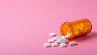 Orange prescription bottle spilled white pills on pink background. Medical healthcare concept for pharmacy, medication, treatment and wellness.