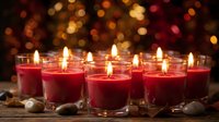 Red candles burning with warm flames creating cozy atmosphere against golden bokeh lights background for holiday celebrations and romantic occasions.