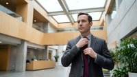 Professional businessman adjusting tie in modern corporate office lobby with natural lighting and contemporary architecture for business concepts.