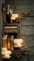 Vintage books stacked with burning candles and purple wildflowers on rustic wooden background creating cozy autumn atmosphere for home decor and relaxation.