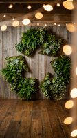 Large succulent wreath with ferns and greenery on rustic wooden wall with warm string lights creating cozy botanical home decor atmosphere.