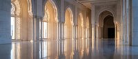 Elegant Islamic architecture corridor with ornate arches and columns reflecting on polished marble floor creating symmetrical patterns in warm lighting.