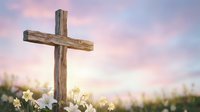 Wooden cross stands in blooming meadow at sunrise with soft pink clouds and warm golden light creating peaceful spiritual atmosphere for Easter worship.