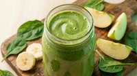 Green smoothie with spinach, banana and apple in glass jar on wooden cutting board for healthy breakfast and detox nutrition.