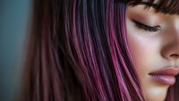 Close up portrait of young Asian woman with pink hair highlights and closed eyes showing natural makeup and serene expression against blurred background.