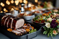 Sliced roasted pork tenderloin on black serving platter with colorful side dishes, fresh salad and floral arrangement against warm bokeh lights background.