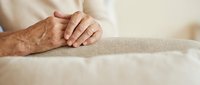 Senior man hands folded on table showing aging skin texture and wrinkles in warm natural lighting for healthcare and elderly care concepts.