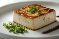 Grilled tofu block with caramelized surface and fresh green herbs on white plate, healthy plant-based protein meal for vegetarian and vegan cooking recipes.