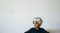 Mature woman with short gray hair wearing a navy blue top and white patterned headwrap, smiling against neutral background. Suitable for lifestyle, diversity, and portrait projects.