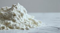 White protein powder heap spilled on wooden surface for fitness nutrition and bodybuilding supplement concepts in kitchen or gym setting.