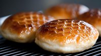 Fresh baked hamburger buns with golden brown tops cooling on wire rack, soft bread rolls for burgers and sandwiches ready for serving at restaurant or home.