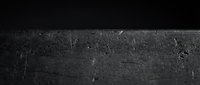 Dark textured asphalt road surface with scratches and wear marks creating dramatic contrast against black background for automotive designs.