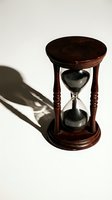 Wooden hourglass with black sand flowing through glass chambers, casting shadow on white background. Concept for time management, deadline, and business productivity.