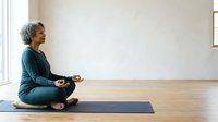 Senior woman with gray hair, East Asian ethnicity, practicing meditation in lotus position on yoga mat in bright, minimalist studio space. Wellness and mindfulness concept.