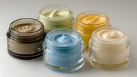 Colorful collection of skincare creams in glass jars, featuring brown, green, blue, yellow, and white cosmetic products arranged on neutral background.
