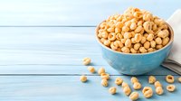 Crunchy honey roasted cereal rings in blue ceramic bowl on rustic wooden background. Scattered breakfast pieces create natural composition for food styling.