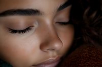 Young woman with closed eyes resting peacefully on soft brown fabric, serene expression showing natural beauty and relaxation in warm lighting.