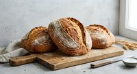 Freshly baked artisan sourdough bread loaves on wooden cutting board in rustic kitchen setting with natural lighting for bakery and food photography.